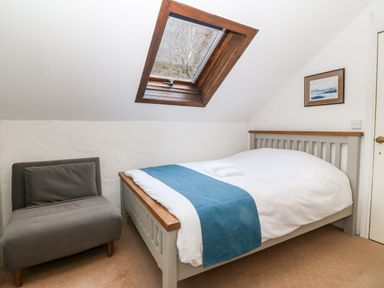 A bedroom with a bed blue runner gray chair and skylight window at Is Y Graig in Beddgelert