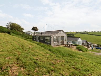 A wooden chalet on a grassy hillside with picnic tables and other chalets in the background at Siesta Chalet Eype Mouth Chalet Park