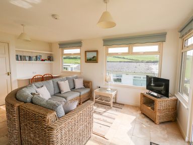 A living room with wicker furniture a TV on a wicker stand a table lamp and a bookshelf at Siesta Chalet in Eype Mouth Chalet Park