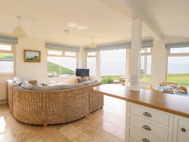 A living room with a wicker sofa a television and windows showing a sea view at Siesta Chalet in Eype Mouth Chalet Park