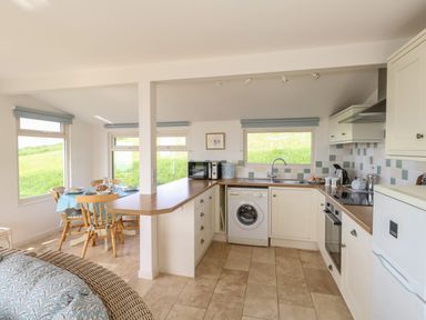 A kitchen with white cabinets and appliances next to a dining table with wooden chairs at Siesta Chalet in Eype Mouth Chalet Park