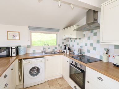 A kitchen with white cabinets wooden countertops a washing machine an oven a microwave and a window at Siesta Chalet in Eype Mouth Chalet Park