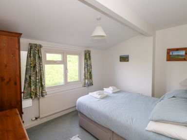 A bedroom with a double bed two folded towels wooden wardrobe and window with patterned curtains at Siesta Chalet in Eype Mouth Chalet Park