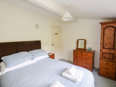 A bedroom with a bed and blue bedding wooden wardrobe and dresser with mirror at Siesta Chalet in Eype Mouth Chalet Park
