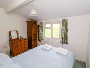 A bedroom with a bed near a window and wooden dresser and wardrobe at Siesta Chalet in Eype Mouth Chalet Park
