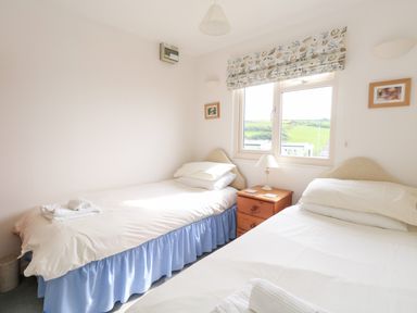 A bedroom with two single beds a wooden nightstand between the beds and a window with floral blinds at Siesta Chalet in Eype Mouth Chalet Park