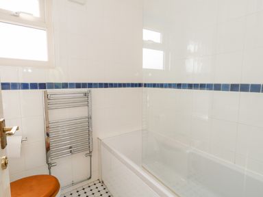 A bathroom with a bathtub glass shower screen heated towel rail and toilet with wooden seat at Siesta Chalet in Eype Mouth Chalet Park
