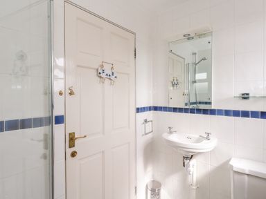 A bathroom with a white door with hooks a sink with a mirror and a shower area at Siesta Chalet in Eype Mouth Chalet Park
