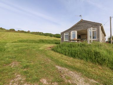 A wooden chalet with open doors and picnic table on a grassy hillside at Siesta Chalet in Eype Mouth Chalet Park
