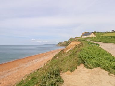 A coastal cliff with a dirt path leading to a building overlooking a beach and sea at Siesta Chalet in Eype Mouth Chalet Park