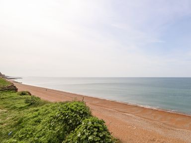 A beach with a sandy shore bordered by greenery and the sea at Siesta Chalet in Eype Mouth Chalet Park