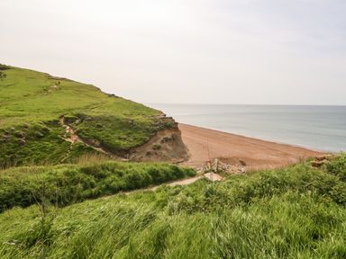 A coastal landscape with grassy hills cliffs a pebble beach and the sea at Siesta Chalet in Eype Mouth Chalet Park