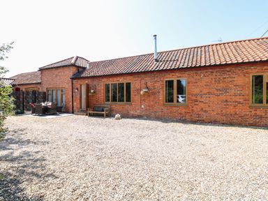 A brick building with tiled roof and gravel ground with outdoor seating at The Barnhouse Felmingham near North Walsham