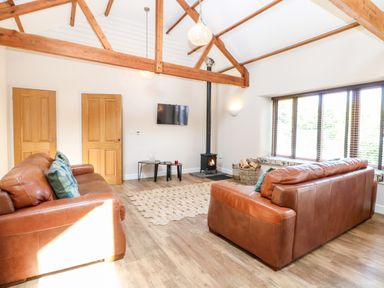 A living room with two brown leather sofas a wood stove a rug and exposed wooden beams at The Barnhouse in Felmingham near North Walsham