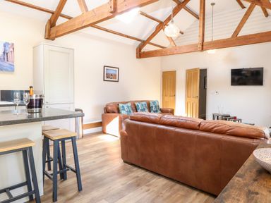 A living room with brown leather sofas wooden beams and a wall-mounted TV at The Barnhouse in Felmingham near North Walsham