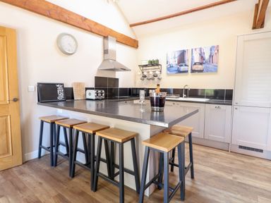 A kitchen with a counter and five stools a sink and a stove at The Barnhouse Felmingham near North Walsham