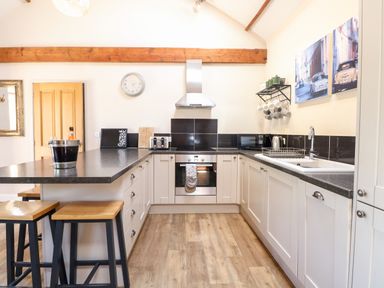 A kitchen with wooden stools black countertops white cabinets and wall art at The Barnhouse Felmingham near North Walsham