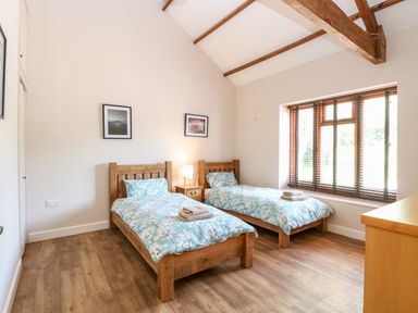 A bedroom with two single beds with blue floral bedding a nightstand with a lamp two framed pictures and a window with blinds at The Barnhouse in Felmingham near North Walsham