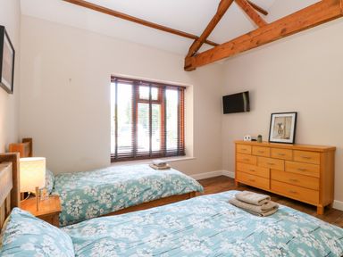 A bedroom with two single beds a wooden dresser and a television on the wall at The Barnhouse Felmingham near North Walsham