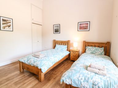 A bedroom with two single wooden beds with blue floral bedding and towels on top at The Barnhouse in Felmingham near North Walsham