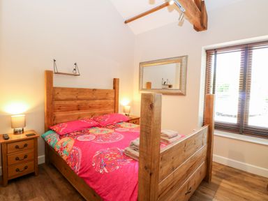 A bedroom with a wooden bed frame red patterned bedding two bedside tables with lamps and a window with wooden blinds at The Barnhouse in Felmingham near North Walsham