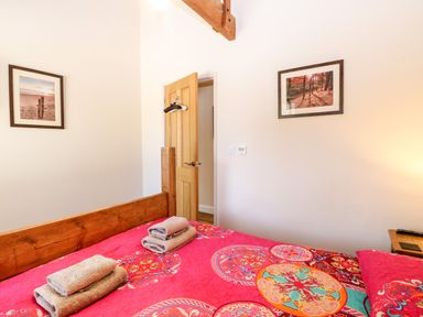 A bedroom with a wooden bed with red patterned bedding two framed pictures on the walls and folded towels on the bed at The Barnhouse in Felmingham near North Walsham