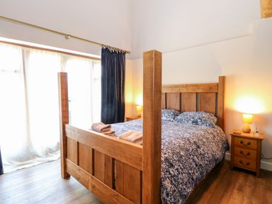 A bedroom with a wooden four-poster bed covered with a floral bedspread and two bedside tables with lamps at The Barnhouse in Felmingham near North Walsham