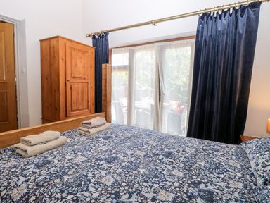 A bedroom with a bed covered in a floral patterned duvet a wooden wardrobe and glass doors with curtains at The Barnhouse in Felmingham near North Walsham