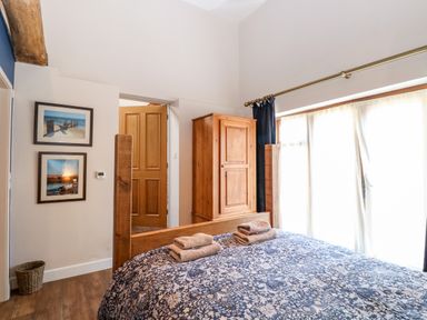 A bedroom with a wooden bed and wardrobe two framed pictures on the wall and a window with curtains at The Barnhouse Felmingham near North Walsham