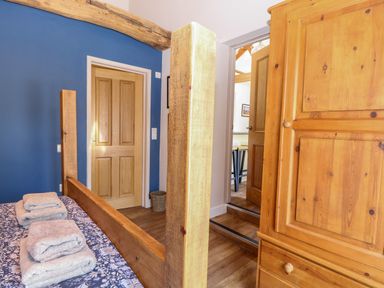 A bedroom with a wooden bed frame, folded towels on the bed, a wooden wardrobe, blue wall and wooden doors at The Barnhouse in Felmingham near North Walsham