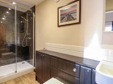 A bathroom with a glass shower enclosure a wooden cabinet and a framed picture on the wall at The Barnhouse Felmingham near North Walsham