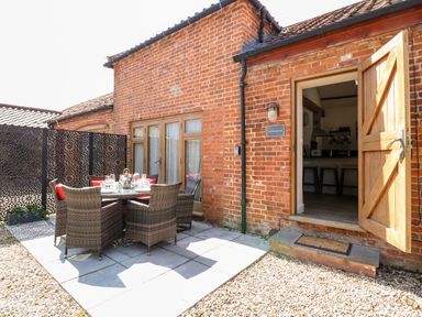 An outdoor dining area with a round table and six wicker chairs on a stone patio at The Barnhouse Felmingham near North Walsham