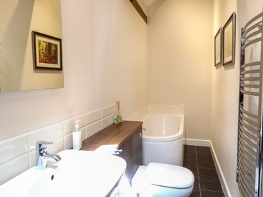 A bathroom with a sink toilet bathtub wooden cabinet mirror and framed pictures at The Barnhouse in Felmingham near North Walsham
