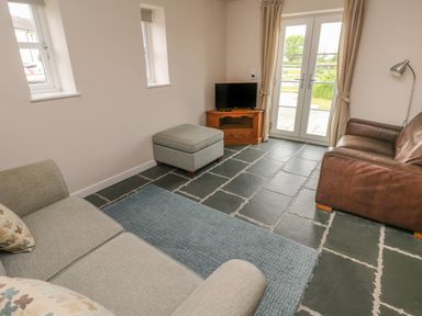 A living room with sofas ottoman television and glass doors at Ystabl Robyn in Llanddarog