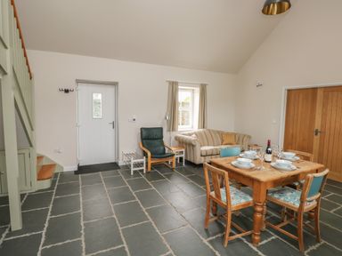 A dining area with a wooden table set for four, a striped sofa, an armchair, and stairs in a room at Ystabl Robyn in Llanddarog