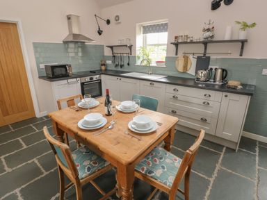 A kitchen with a wooden dining table set for four and white cabinets at Ystabl Robyn in Llanddarog
