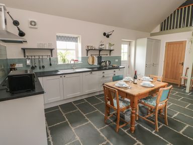 A kitchen with white cabinets a wooden dining table set for four a microwave and kitchen utensils at Ystabl Robyn in Llanddarog