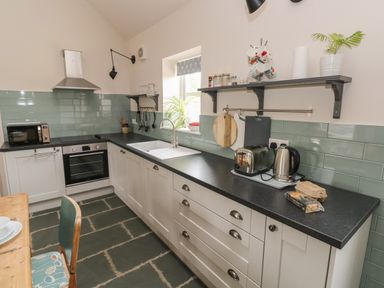 A kitchen with white cabinets a black countertop a toaster a kettle and utensils on shelves at Ystabl Robyn in Llanddarog