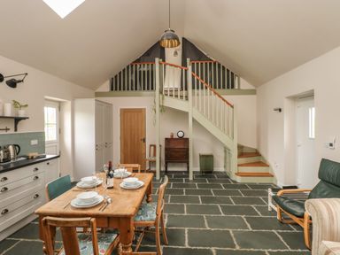 A kitchen and dining area with a wooden table set for four under a staircase with a loft at Ystabl Robyn in Llanddarog