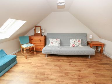 A room with a gray sofa, wooden chest of drawers, wooden chair, wooden side table, and a skylight window at Ystabl Robyn in Llanddarog