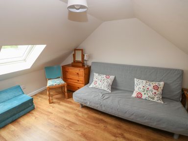 A room with a grey sofa with floral cushions a wooden chest of drawers a blue chair and a skylight window at Ystabl Robyn in Llanddarog