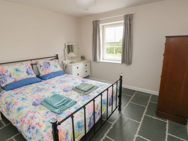 A bedroom with a double bed with colorful bedding a white dresser with a mirror and a wooden wardrobe at Ystabl Robyn in Llanddarog