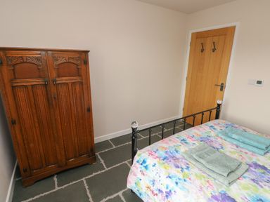 A bedroom with a wooden wardrobe a bed with a floral bedspread and folded towels on stone tile flooring at Ystabl Robyn in Llanddarog