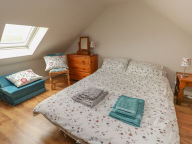 A bedroom with a double bed folded towels a wooden chest of drawers a chair and a skylight window at Ystabl Robyn in Llanddarog