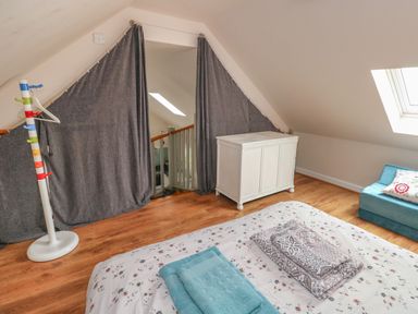 A bedroom with a bed with folded towels, a colorful coat rack, a white cabinet, and a small sofa near a skylight window at Ystabl Robyn in Llanddarog
