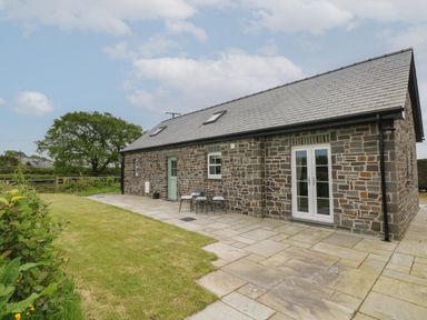 A stone house with a slate roof and patio area with table and chairs at Ystabl Robyn in Llanddarog
