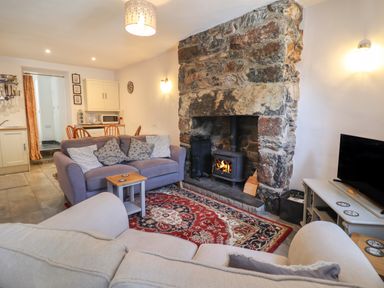 A living room with two sofas a stone fireplace and a dining area at Llygoden Cottage in Beddgelert