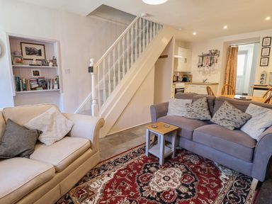 A living room with two sofas a red patterned rug and a staircase leading to the upper floor at Llygoden Cottage in Beddgelert
