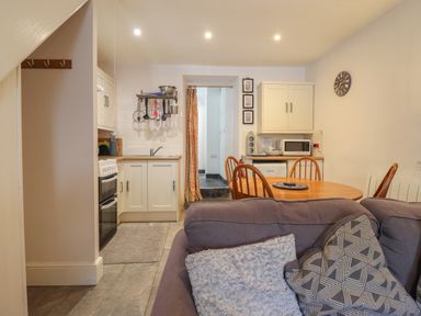 A kitchen and dining area with white cabinets wooden table and chairs and a gray sofa at Llygoden Cottage in Beddgelert