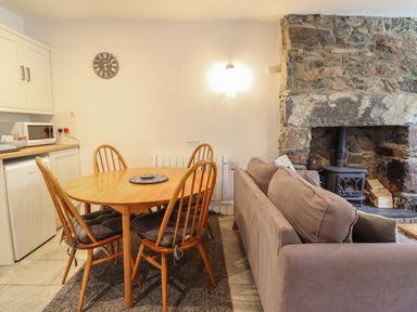 A kitchen dining area with wooden table and chairs next to a brown sofa and stone fireplace at Llygoden Cottage in Beddgelert